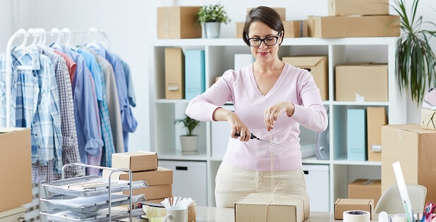 Young woman working at a small fashion business, cutting thread on a parcel, representing global supply chain operations and production efficiency with SAP S/4HANA Fashion