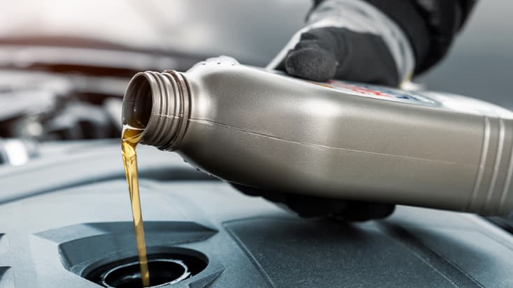 A person pouring engine oil into a car, representing automotive service operations and efficiency improvements enabled by SAP Datasphere.